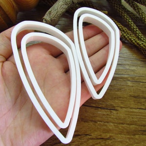 May include: A set of three white plastic cookie cutters shaped like a teardrop. The cutters are nested inside each other, with the largest cutter on the outside and the smallest cutter on the inside.