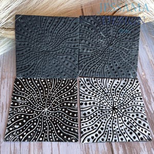 May include: Four square coasters featuring a radial pattern of raised dots and swirling lines. Two coasters are solid matte black, while the other two are black with white highlights that emphasize the textured, sunburst-like design on each surface.