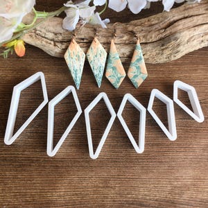 May include: Four diamond-shaped earrings with a marbled peach and teal pattern on copper-toned hooks, accompanied by six white plastic diamond-shaped cutters of varying sizes arranged in a row below the jewelry pieces.