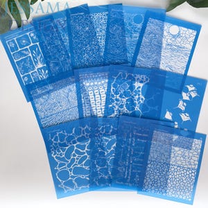 Op de afbeelding: Een verzameling blauwe sjablonen met diverse witte ontwerpen, waaronder bloempatronen, geometrische vormen en abstracte kunst. De sjablonen zijn in een waaier gerangschikt, wat de verscheidenheid aan ontwerpen voor knutsel- en kunstprojecten laat zien.