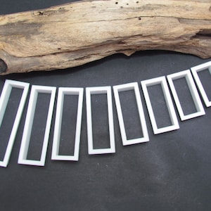 May include: Nine white plastic rectangular frames of varying sizes arranged in a semi-circle on a black surface.