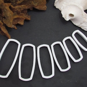 May include: A set of eight white plastic cookie cutters shaped like elongated ovals. The cutters are arranged in a semi-circle on a black surface.