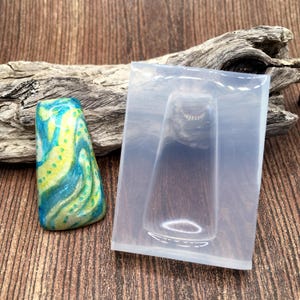 May include: A clear silicone mold for making resin pendants. The mold is shaped like a teardrop with a small hole at the top for a bail. The mold is shown next to a finished resin pendant with a blue, green, and yellow marbled design.