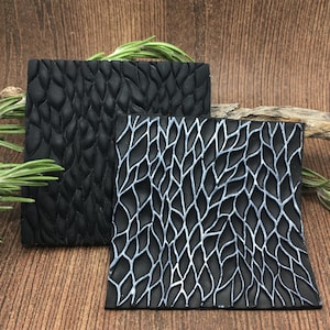 May include: Two black silicone texture mats with raised leaf patterns. One mat has a dark gray leaf pattern and the other has a light gray leaf pattern.
