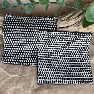 May include: Two square ceramic dishes featuring a textured surface with a repeating pattern of small white dots on a black background. The dishes have slightly curved edges and a hand-crafted appearance, displaying a high-contrast monochrome design.