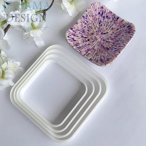 May include: A white set of square-shaped cookie cutters and a decorative dish. The dish has a speckled purple and white design. The image also includes the text "JENAMA DESIGN".