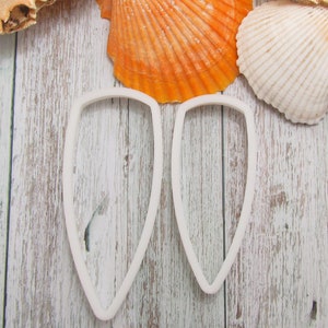 May include: Two white plastic cookie cutters shaped like seashells. The cutters are on a whitewashed wooden surface.