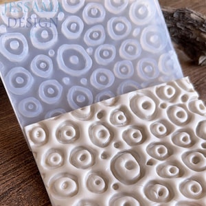 May include: A close-up of a silicone mold and a cast piece. The mold is transparent and features a pattern of concentric circles. The cast piece is off-white and shows the same circular design. The text "JESSAMA DESIGN" is visible on the mold.