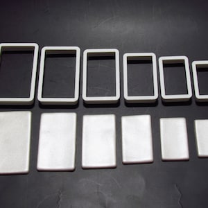 Può includere: Un set di dieci cornici rettangolari in plastica bianca di diverse dimensioni. Le cornici sono disposte su due file, con le cornici più grandi nella fila superiore e le cornici più piccole nella fila inferiore.