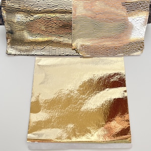 Può includere: Primo piano di vari fogli metallici con superfici strutturate e riflettenti. I fogli mostrano tonalità oro, bronzo e argento, con un motivo screpolato su alcuni. L'immagine mostra le diverse trame e colori dei materiali.