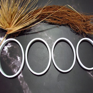 May include: Four white rubber bands arranged in a row on a dark grey background. The rubber bands are circular and have a smooth surface.