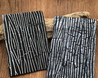 May include: Two rectangular panels featuring a raised, textured surface pattern resembling vertical bamboo stalks. One panel is primarily black with white highlights, while the other is silver with black recessed grooves.