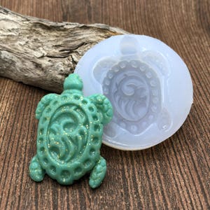 May include: A green turtle-shaped silicone mould with a detailed design. The mould is used to create resin or polymer clay jewellery.