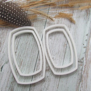 May include: Two white plastic oval-shaped cookie cutters, one slightly larger than the other, on a whitewashed wood surface.