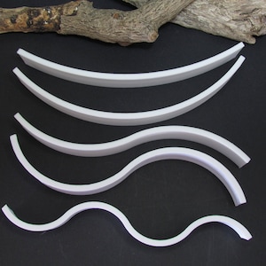 May include: Five white flexible plastic strips of varying lengths and curves, arranged in a graduated pattern on a black background.