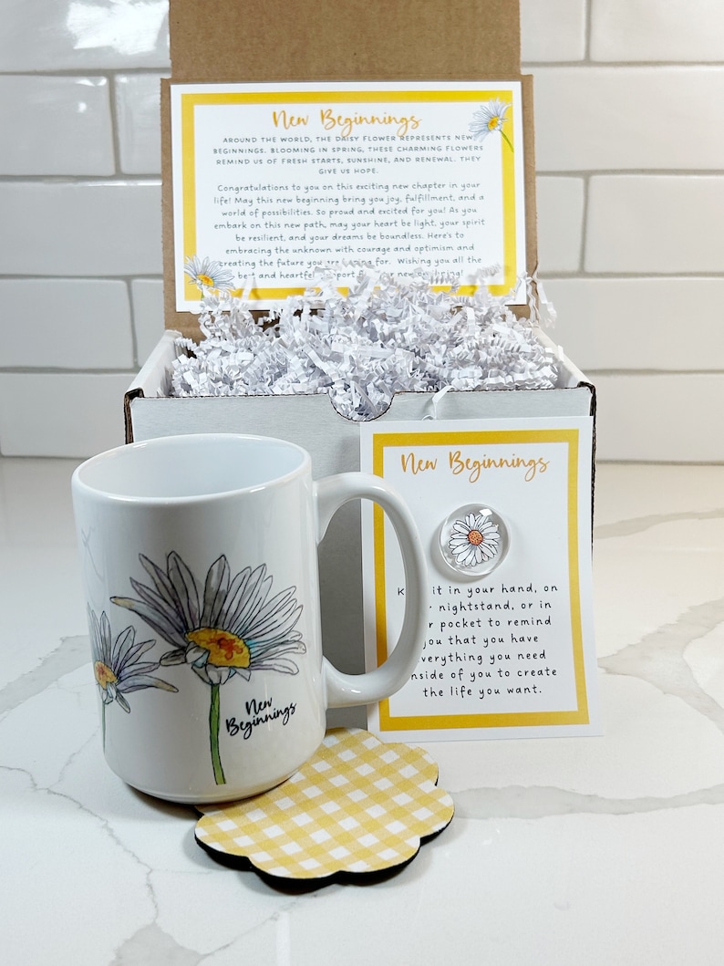Pu&ograve; includere: Una tazza bianca con un disegno di margherita gialla e bianca e il testo "New Beginnings". La tazza &egrave; appoggiata su un sottobicchiere a scacchi giallo e bianco. C'&egrave; un piccolo biglietto con il testo "New Beginnings" e un disegno di margherita.