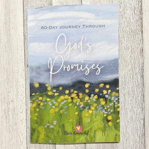 May include: A book cover with the title "God's Promises" in elegant script. The cover features a watercolor landscape with a field of yellow and purple flowers, a blue sky, and the text "60-Day Journey Through". The artist's name is "Stacie Kearns Art".