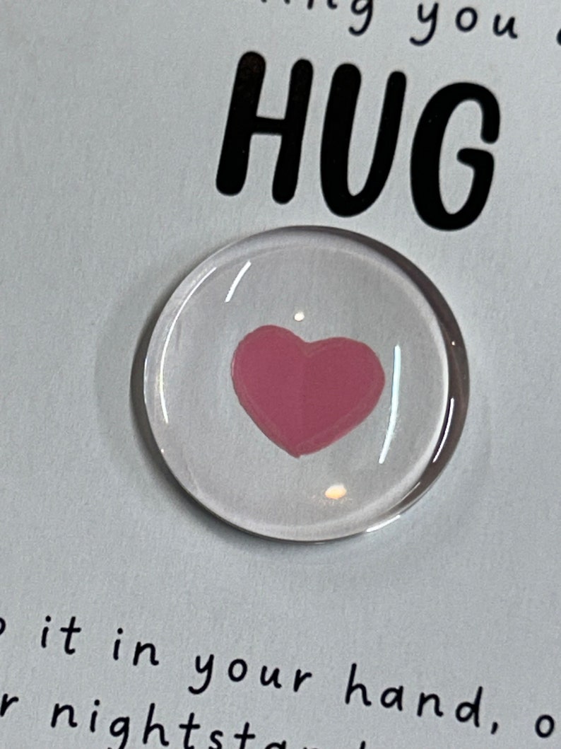 Puede incluir: Un peque&ntilde;o c&iacute;rculo de vidrio con un coraz&oacute;n rosa en su interior. El texto "Sending you a HUG" es visible en el fondo.
