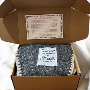 May include: A gray and white throw blanket with a white label that reads "The Lord will stand with you and give you Strength. 2 Timothy 4:17". The blanket is in a brown cardboard box.