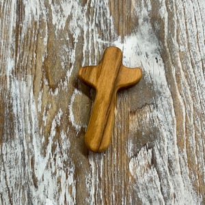 May include: A small, wooden cross with a natural wood finish. The cross is made of a light brown wood and has a simple, rustic design.