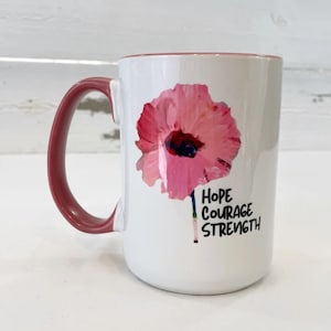 May include: White ceramic mug with a pink poppy flower design and the words "Hope Courage Strength" printed on the side. The mug has a red handle.