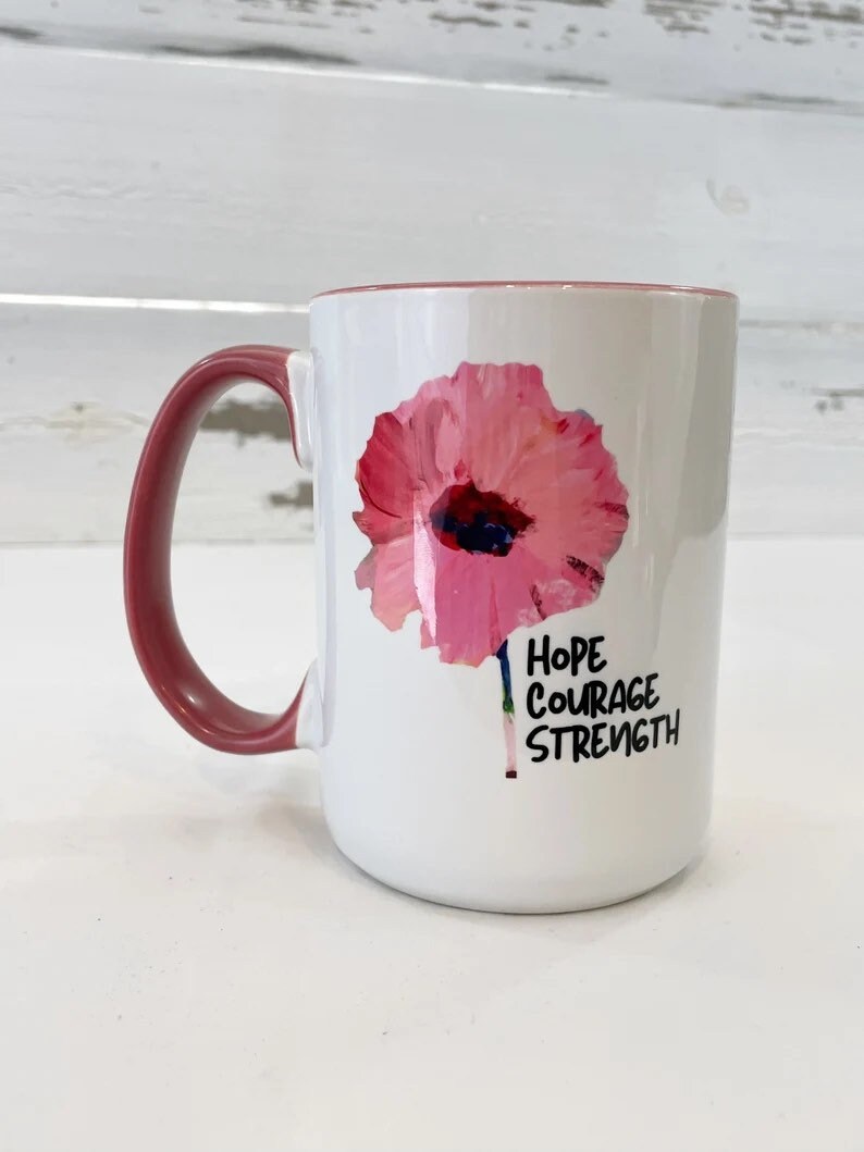 May include: White ceramic mug with a pink poppy flower design and the words "Hope Courage Strength" printed on the side. The mug has a red handle.