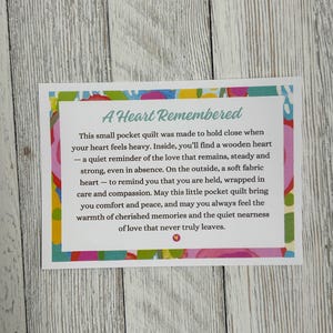 May include: A small pocket quilt with a colorful floral pattern. The text reads "A Heart Remembered" and includes a message about love and remembrance.