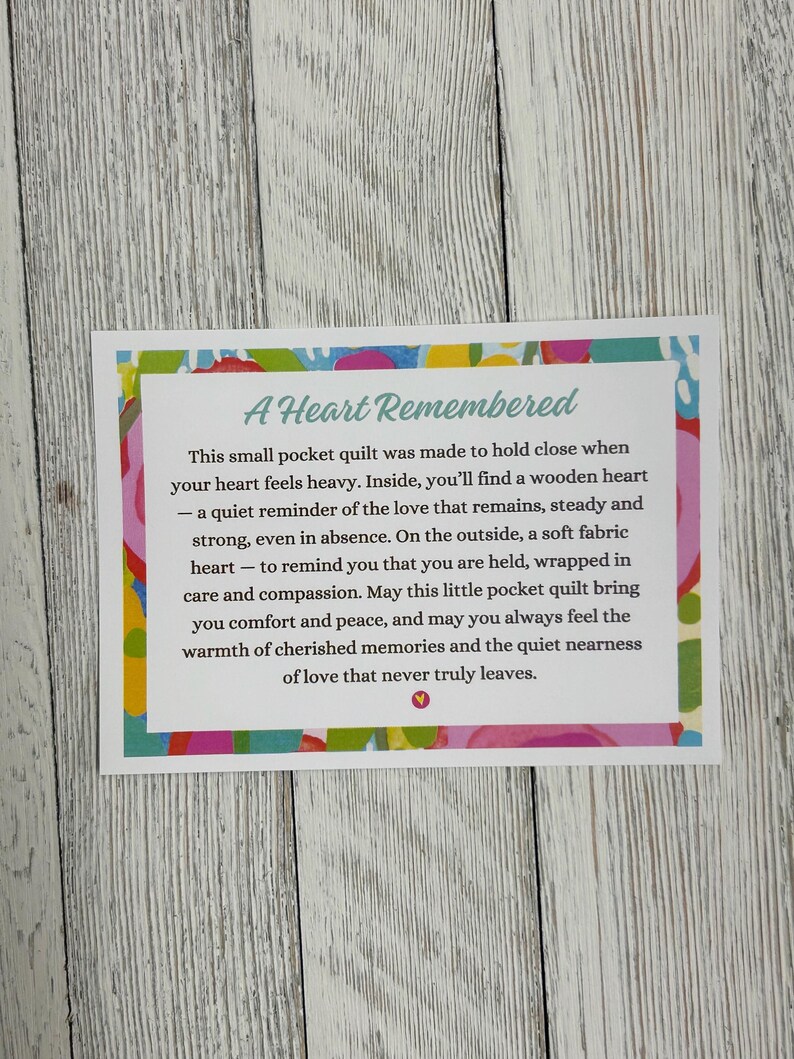 May include: A small pocket quilt with a colorful floral pattern. The text reads "A Heart Remembered" and includes a message about love and remembrance.