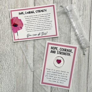 May include: Two pink cards with inspirational messages about hope, courage, and strength. The cards feature a red poppy flower and a small red heart. The text on the cards reads: "You are strong, you are loved, and you are not defined by this diagnosis. Embrace each step forward, celebrate the small victories, and remember that you possess an incredible resilience within you. Though the road ahead may be challenging, you are not alone in this fight. Every day is a step forward on your journey to healing, may your strength, hope, and positivity continue to guide you toward brighter days. You can do this!" and "Keep it in your hand, on your nightstand, or in your pocket to remind you that you are strong, loved, and not alone! You CAN do this!"