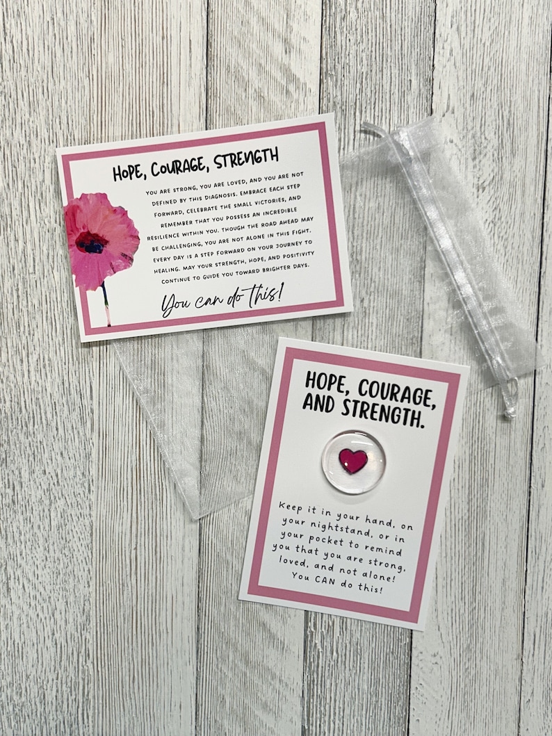 May include: Two pink cards with inspirational messages about hope, courage, and strength. The cards feature a red poppy flower and a small red heart. The text on the cards reads: "You are strong, you are loved, and you are not defined by this diagnosis. Embrace each step forward, celebrate the small victories, and remember that you possess an incredible resilience within you. Though the road ahead may be challenging, you are not alone in this fight. Every day is a step forward on your journey to healing, may your strength, hope, and positivity continue to guide you toward brighter days. You can do this!" and "Keep it in your hand, on your nightstand, or in your pocket to remind you that you are strong, loved, and not alone! You CAN do this!"
