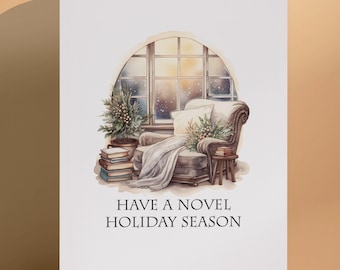 May include: A white greeting card featuring a watercolor illustration of an armchair, a stack of books, and a small evergreen tree by a window. The text "HAVE A NOVEL HOLIDAY SEASON" is printed in black capital letters at the bottom of the card.