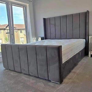 May include: A grey upholstered bed frame with a tall headboard featuring vertical channel tufting. The bed frame has a platform base and a mattress.