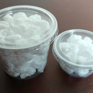 May include: Two clear plastic containers with lids, one large and one small, filled with white, fluffy material. The containers are on a dark brown surface. The lids are transparent.