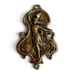 Peut inclure: Une plaque en métal de couleur bronze présentant un bas-relief d'une figure ailée en mouvement. La figure porte un casque et des vêtements fluides, un bras levé. La plaque a une forme organique irrégulière avec une boucle en haut et en bas.