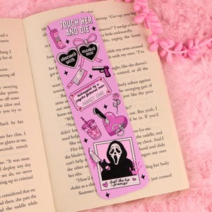 Op de afbeelding: Een roze boekenlegger met horror-illustraties, waaronder een telefoon, harten met de tekst "obsessed with masked men", een hakmes, een pistool, een ticket met "kidnapped by a psycho fictional man", een roos, een drankje en een spookfiguur.