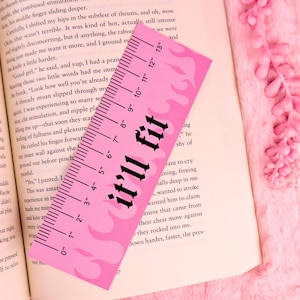 Op de afbeelding: Roze liniaal met zwarte tekst "it'll fit" en vlamontwerpen. De liniaal is 33 cm lang en ligt op een open boek.