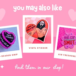 Op de afbeelding: Drie verschillende producten: een roze en zwarte e-reader grip met de tekst "I eat that shit up" en "dark romance", een vinyl sticker met een rood hart en de tekst "I want to play a game", en een roze luchtverfrisser met de tekst "this car is fueled by SMUT".