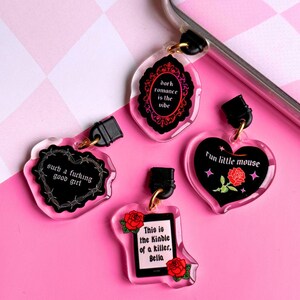 K&ouml;nnte beinhalten: Vier Acryl-Anh&auml;nger mit schwarzem Text und goldfarbener Hardware. Die Anh&auml;nger haben die Form eines Herzens, einer Flasche und einer dekorativen Form. Der Text lautet "dark romance is the vibe", "such a fucking good girl", "Fun little mouse" und "This is the Kindle of a killer, Bella".