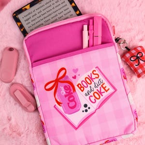 Può includere: Custodia per libri a quadri rosa e bianchi con grafica di lattina di Diet Coke e libro. Il testo sul libro recita "BOOKS and diet COKE". La custodia contiene un Kindle e penne rosa. Sono visibili anche una luce da lettura rosa e un portachiavi.