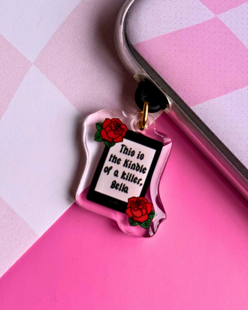 May include: A clear plastic charm with a black and white image of a Kindle and the text "This is the Kindle of a killer, Bella". The charm is decorated with red roses.