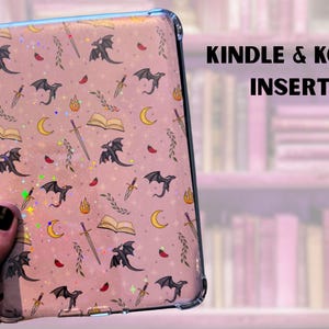 May include: A clear plastic case with a pink background and a repeating pattern of black dragons, swords, open books, and crescent moons. The text "KINDLE & KOBO INSERT" is printed in black at the top of the image.