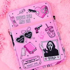Può includere: Una custodia rettangolare rosa per tablet con varie illustrazioni grafiche tra cui un cuore, un coltello, manette, una pistola, una bevanda, un libro e una figura mascherata. Il testo recita TOUCH HER AND DIE, obsessed with masked men e ADMIT ONE.