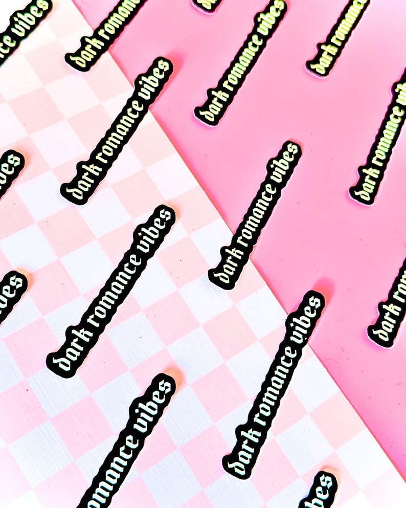 May include: A collection of stickers with the text "dark romance vibes" in a gothic font. The stickers are on a pink and white checkered background.