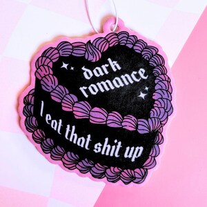K&ouml;nnte beinhalten: Rosaer Auto-Lufterfrischer in Form eines Kuchens mit schwarzem Frosting und lila und rosa Streuseln. Der Text auf dem Frosting lautet "dark romance I eat that shit up".