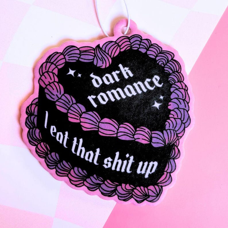 K&ouml;nnte beinhalten: Rosaer Auto-Lufterfrischer in Form eines Kuchens mit schwarzem Frosting und lila und rosa Streuseln. Der Text auf dem Frosting lautet "dark romance I eat that shit up".