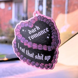 K&ouml;nnte beinhalten: Rosaer Auto-Lufterfrischer in Herzform mit schwarzem und violettem Design. Es steht "dark romance I eat that shit up" in gotischer Schrift.