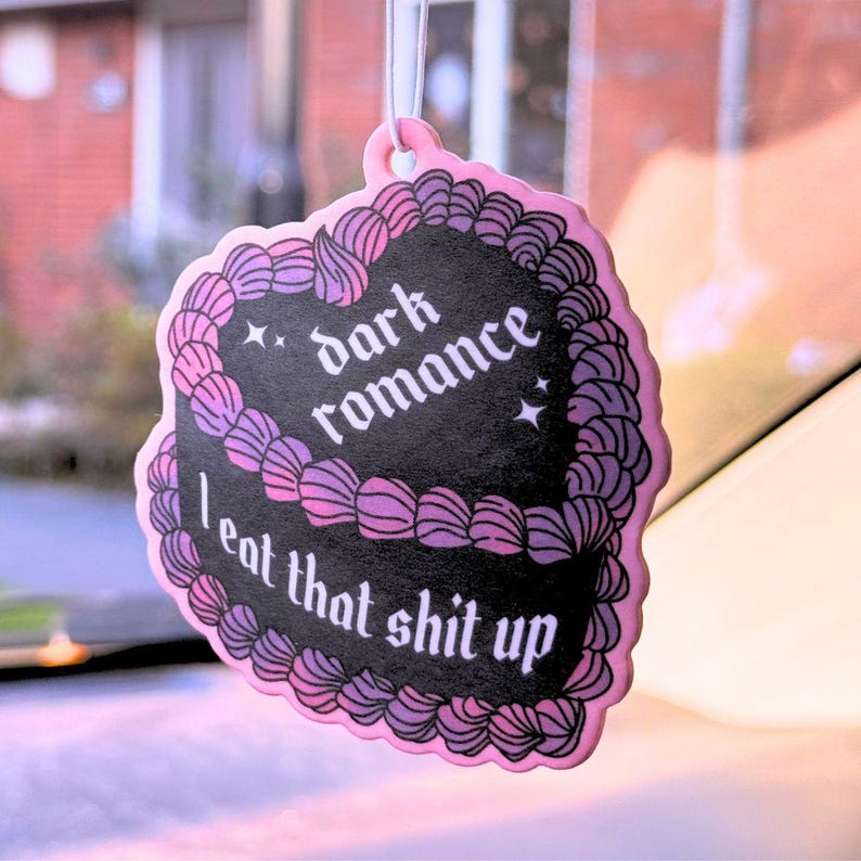 K&ouml;nnte beinhalten: Rosaer Auto-Lufterfrischer in Herzform mit schwarzem und violettem Design. Es steht "dark romance I eat that shit up" in gotischer Schrift.