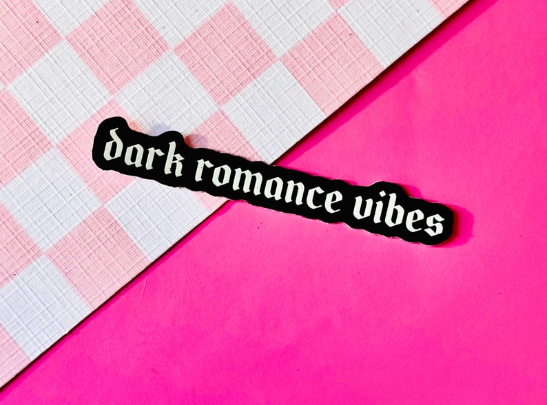 May include: Black sticker with white text that reads "dark romance vibes" on a pink and white checkered background.