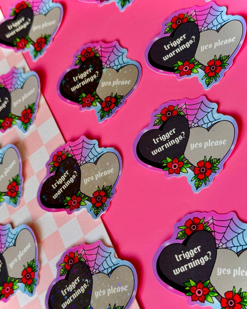 May include: Two heart-shaped stickers with a spiderweb design. One heart is black with the text "trigger warnings?" and the other heart is white with the text "yes please".