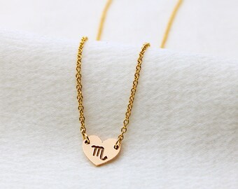 May include: A gold chain necklace with a heart pendant featuring the zodiac symbol for Scorpio.